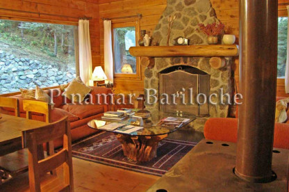 Complejo de Cabañas en alquiler con costa en Lago Gutierrez. Capacidad 7 personas. Living con confortables sillones y estufa hogar revestida en piedra en Bariloche.