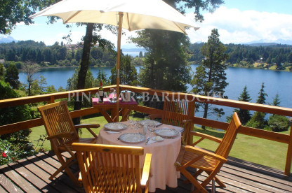 Casa en alquiler en Lago Moreno, predio con casa o cabaña para 4 que pueden sumarse a la capacidad de la casa. Balcón terraza al lago con mesa y sombrilla en Bariloche