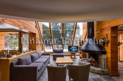 Living de chalet en alquiler en Villa La Angostura, con hogar a leña y amplios ventanales con vista al bosque. Living con hogar y ventanales en chalet de Villa La Angostura