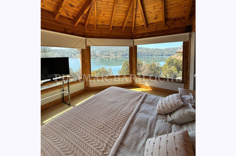Dormitorio principal en suite, cama king, enmarcado por grandes ventanales al lago.